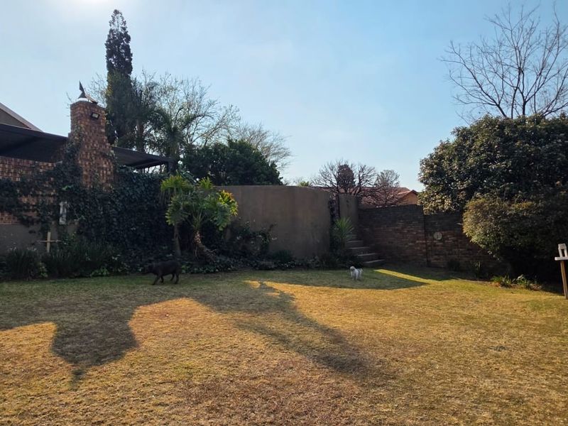 Spacious rear garden featuring a brick chimney, covered patio area, and stone stairs leading to a raised section of the yard.