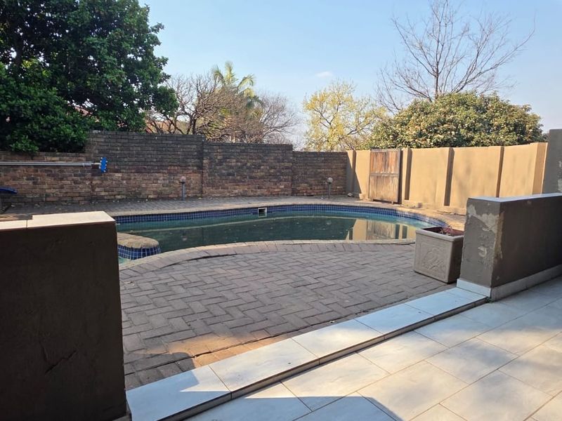 Outdoor pool area featuring a paved surround, tiled patio space, and brick boundary walls, requiring some maintenance and cosmetic updates.