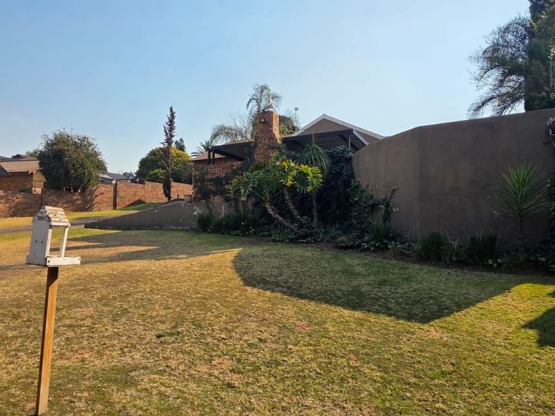 A spacious backyard garden featuring a lawn, concrete stairs, and a brick chimney structure, showing signs of dry vegetation and weathered exterior finishes.