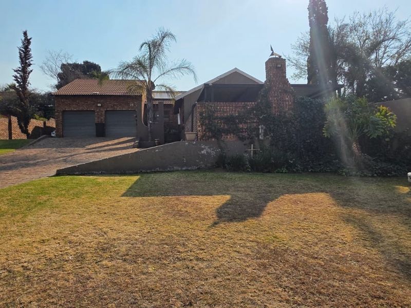 Front view of a brick house featuring a double garage, paved driveway, and a large front lawn with a retaining wall.