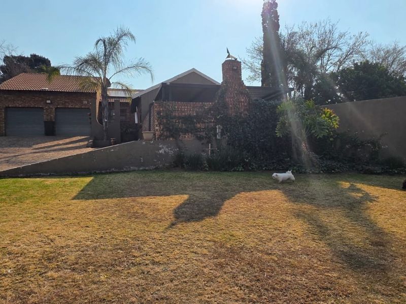 Front view of a residential property featuring a double garage, brick chimney, and a paved driveway with a surrounding boundary wall.