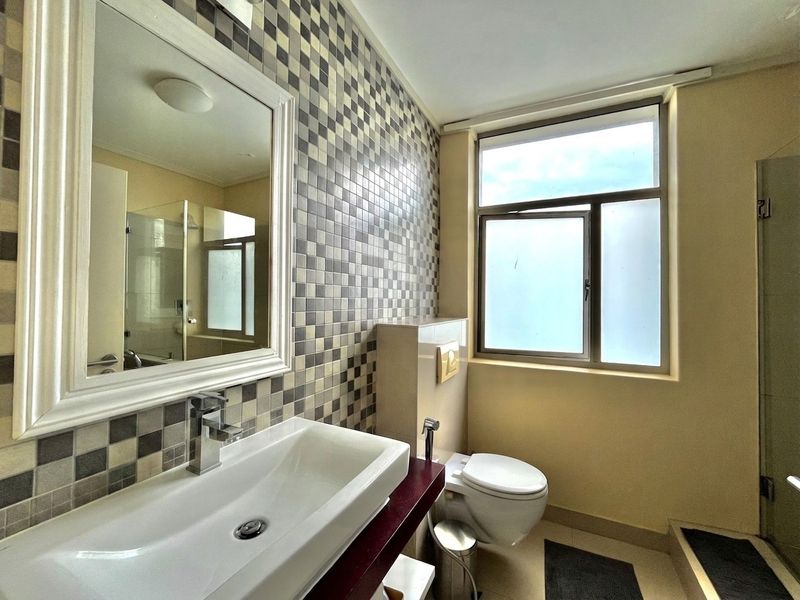 A modern bathroom featuring a mosaic tile accent wall, wall-mounted vanity basin, concealed cistern toilet, and a separate shower enclosure with frosted window.