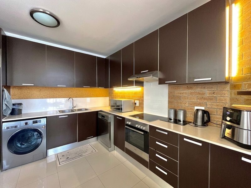 Modern kitchen featuring dark cabinetry, stainless steel appliances, integrated oven, electric cooktop, and a stylish exposed brick backsplash with under-cabinet lighting.