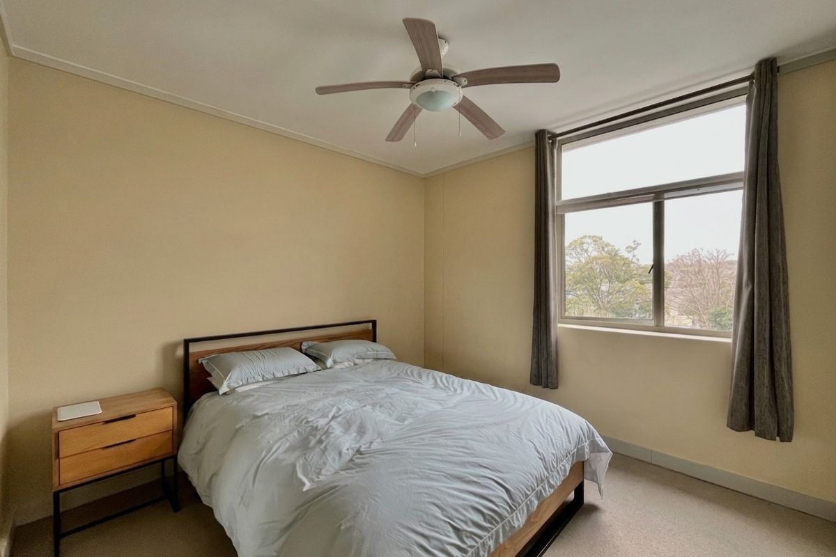 A well-lit bedroom featuring a ceiling fan and a large window with views, providing a comfortable and functional living space.