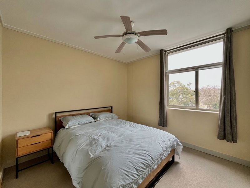 A well-lit bedroom featuring a ceiling fan and a large window with views, providing a comfortable and functional living space.
