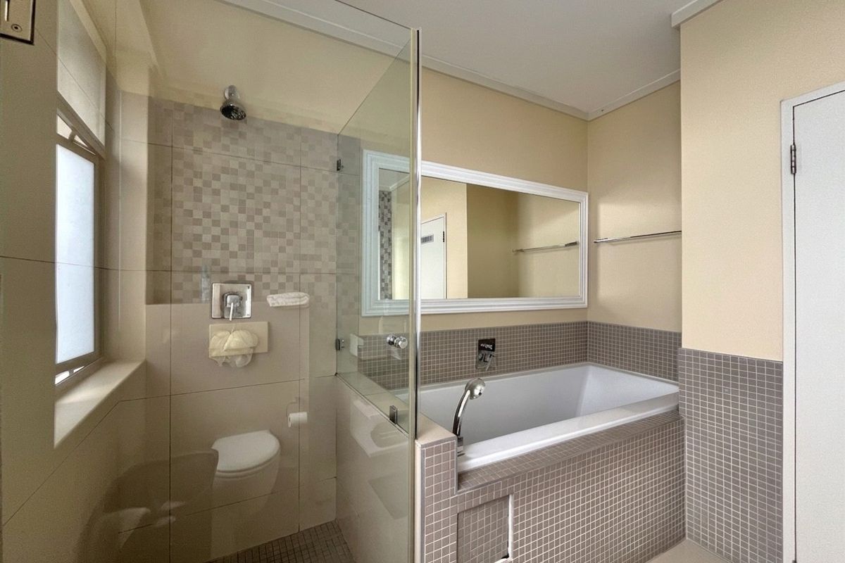 A clean, modern bathroom featuring a built-in bathtub, a glass-enclosed shower area, and neutral mosaic tiling throughout.