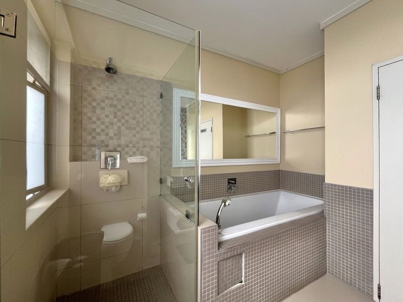 A clean, modern bathroom featuring a built-in bathtub, a glass-enclosed shower area, and neutral mosaic tiling throughout.