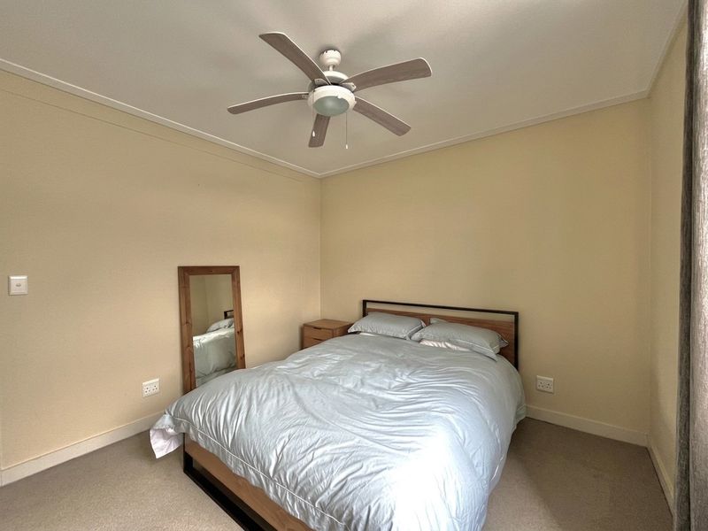 A neutrally painted bedroom featuring a ceiling fan, carpeted flooring, and standard electrical fixtures, offering a clean and functional living space.