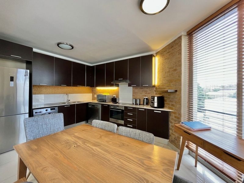 Modern open-plan kitchen featuring dark cabinetry, built-in appliances, and an exposed brick feature wall, seamlessly integrated with the dining area.