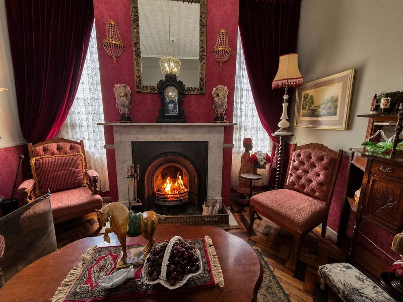 A traditional living room featuring a prominent fireplace with a marble mantelpiece, ornate wall sconces, and classic parquet flooring.