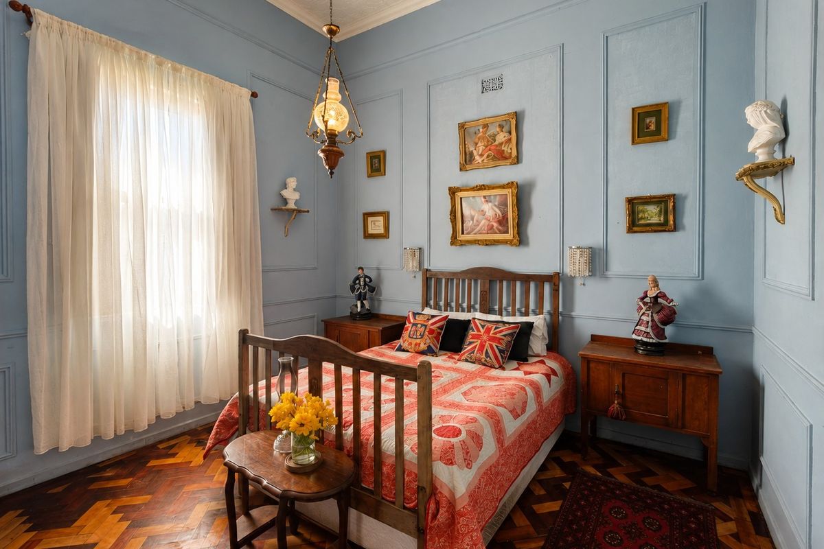 A well-maintained bedroom featuring classic herringbone timber flooring, decorative wall paneling, and high ceilings with period-style architectural details.