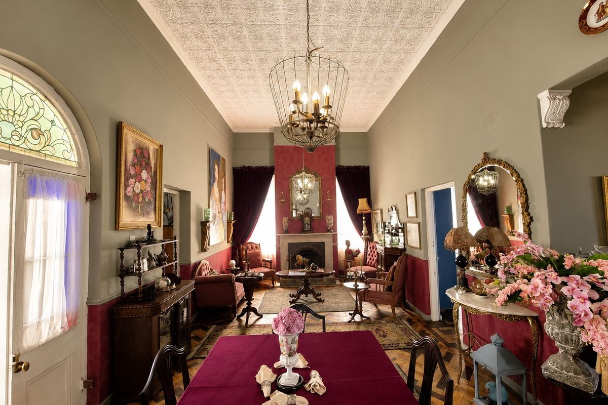 Elegant living room featuring a classic pressed metal ceiling, original parquet flooring, a central fireplace, and a beautiful arched stained glass window.