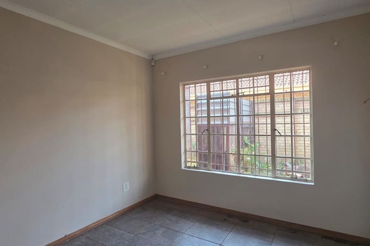 An empty bedroom featuring tiled flooring, security bars on the window, and neutral wall paint, ready for personalization.