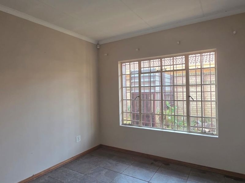 An empty bedroom featuring tiled flooring, security bars on the window, and neutral wall paint, ready for personalization.