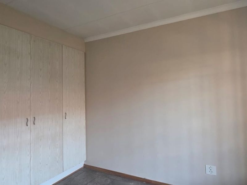 A clean, empty bedroom featuring neutral walls, tiled flooring, and built-in wooden cupboards, offering a blank canvas for personalization.