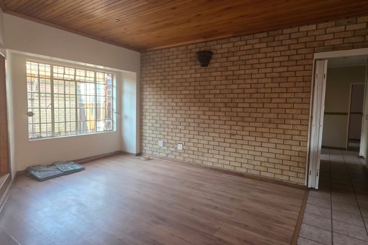 Spacious living area featuring an exposed brick feature wall, timber ceiling, and laminate flooring, offering a blank canvas for modern interior updates.