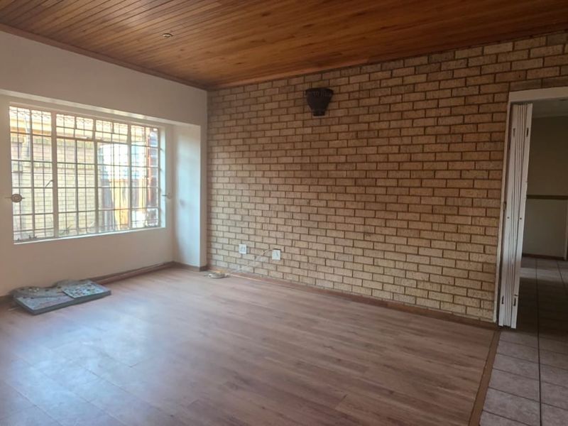 Spacious living area featuring an exposed brick feature wall, timber ceiling, and laminate flooring, offering a blank canvas for modern interior updates.