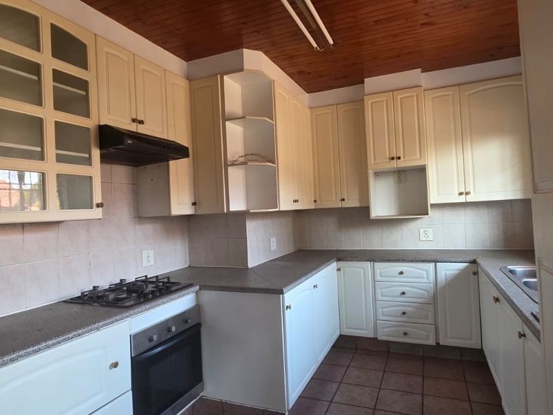 A functional kitchen featuring built-in cabinetry, gas hob, oven, extractor fan, and tiled backsplash, offering a practical layout ready for modernization.