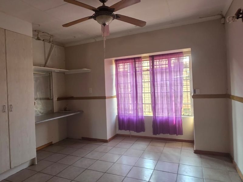 A vacant bedroom featuring built-in cupboards, tiled flooring, a ceiling fan, and security bars on the window.