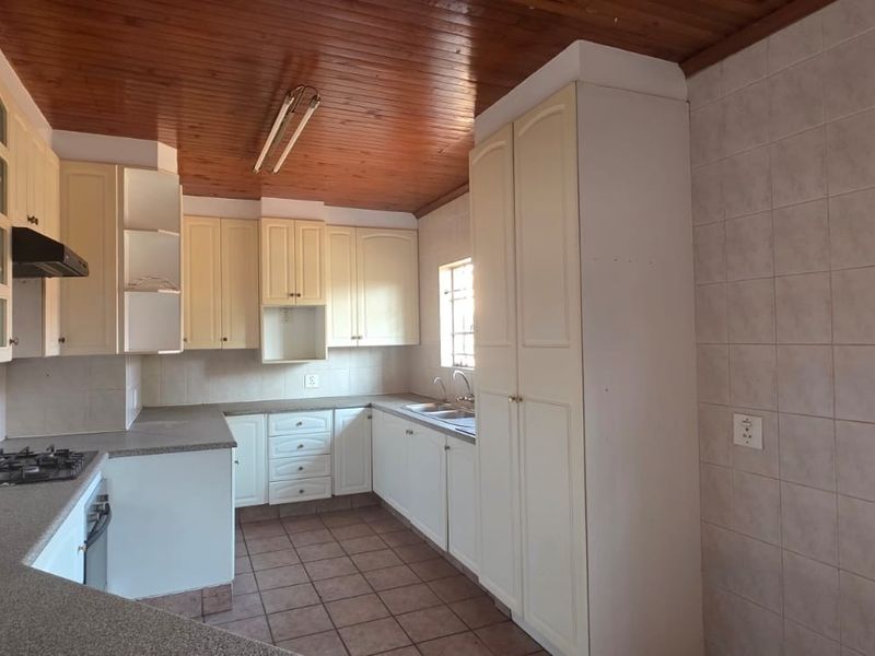 A functional kitchen featuring built-in cabinetry, a gas hob, oven, extractor fan, and double sink, finished with tiled flooring and a timber ceiling.