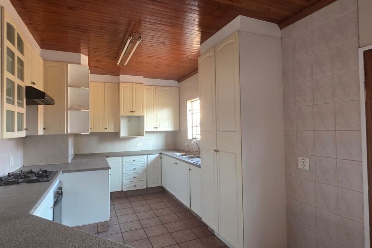 A functional kitchen featuring built-in cabinetry, a gas hob, oven, extractor fan, and double sink, finished with tiled flooring and a timber ceiling.