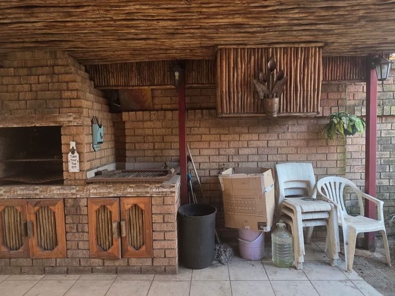 Covered outdoor patio area featuring a built-in brick braai, thatched ceiling, and tiled flooring, providing a functional space for outdoor entertaining.