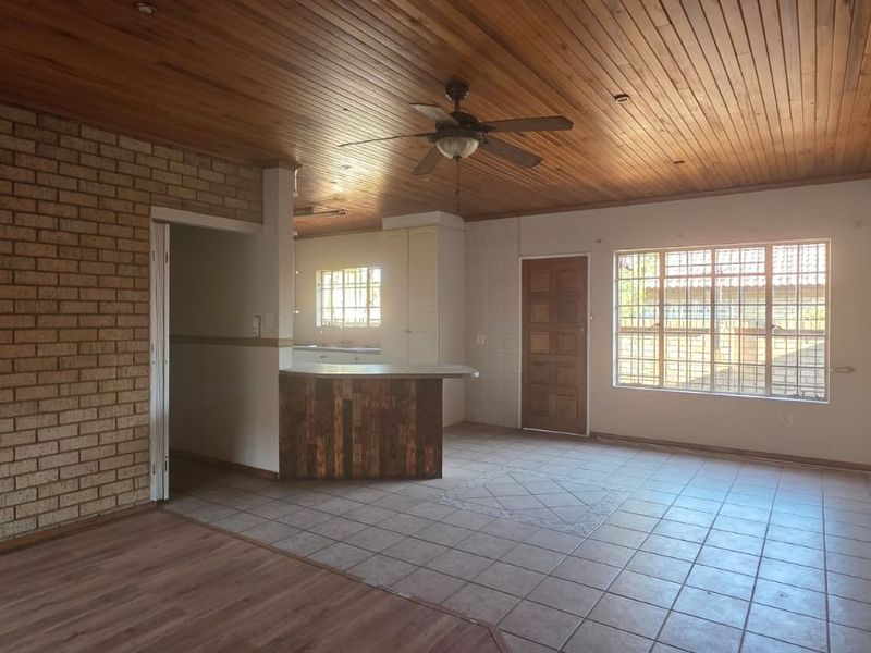 Spacious open-plan living area featuring a timber ceiling, exposed brick feature wall, and a breakfast bar connecting to the kitchen space.