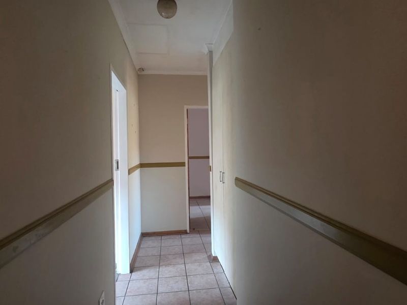 A vacant hallway featuring tiled flooring, built-in storage cupboards, and decorative dado rails, providing access to adjacent rooms.