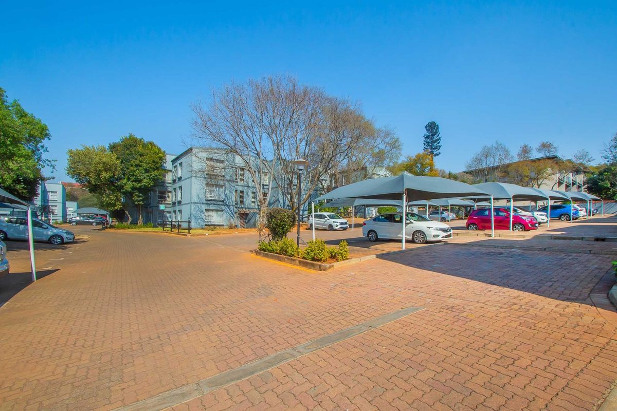 Exterior view of the apartment complex parking area featuring paved driveways and covered shade cloth parking bays.