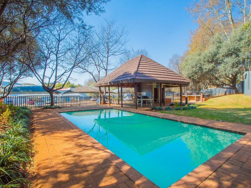 Outdoor pool area featuring a rectangular swimming pool, brick paved surround, and a covered thatched gazebo with built-in braai facilities.