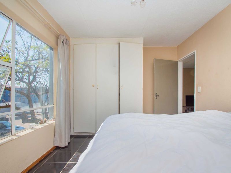 A bedroom featuring built-in cupboards, tiled flooring, and a large window providing natural light and exterior views.