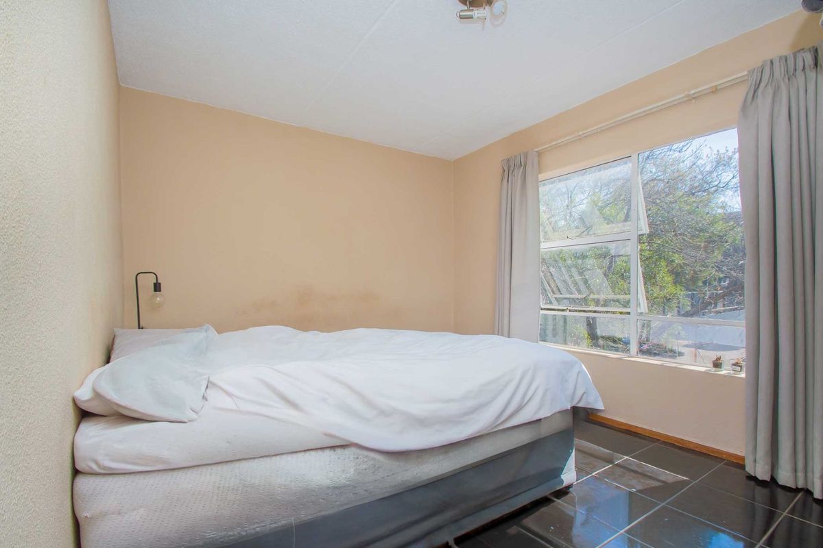 A bedroom featuring dark tiled flooring and a large window, currently showing signs of wall staining and requiring cosmetic updates.