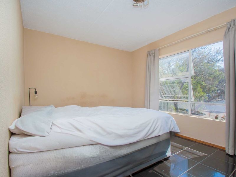 A bedroom featuring dark tiled flooring and a large window, currently showing signs of wall staining and requiring cosmetic updates.