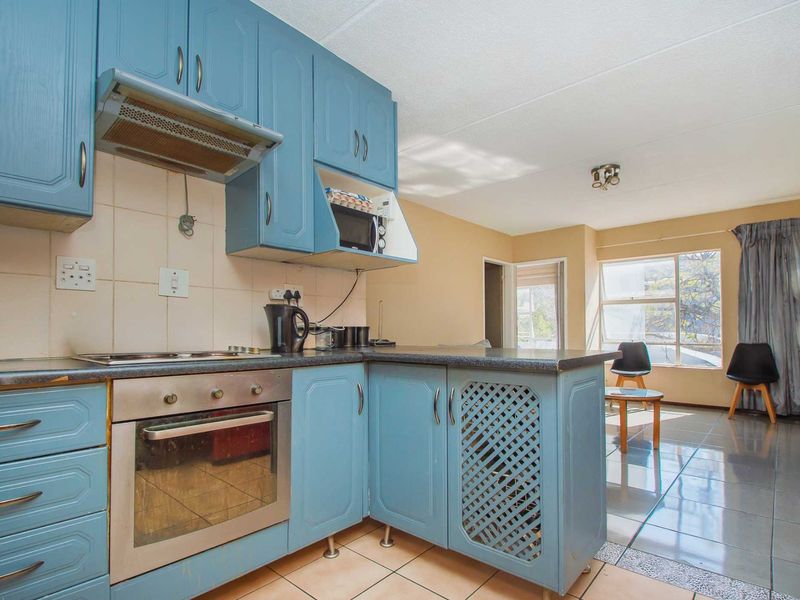 Open-plan kitchen and living area featuring blue cabinetry, built-in oven, hob, and tiled flooring, offering a functional layout with natural light.