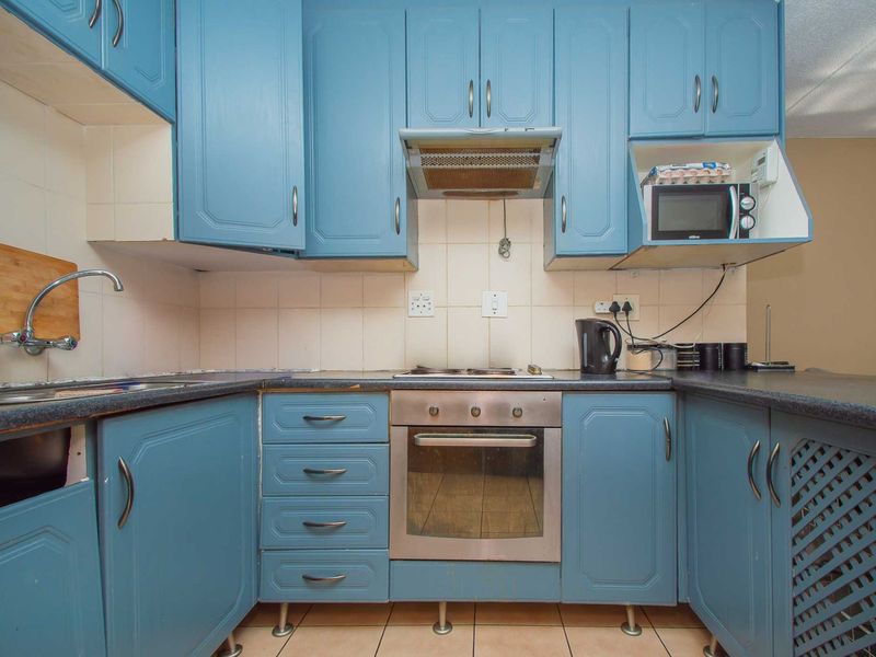 A functional kitchen featuring blue cabinetry, laminate countertops, a built-in oven, and a tiled backsplash, offering potential for a modern cosmetic update.