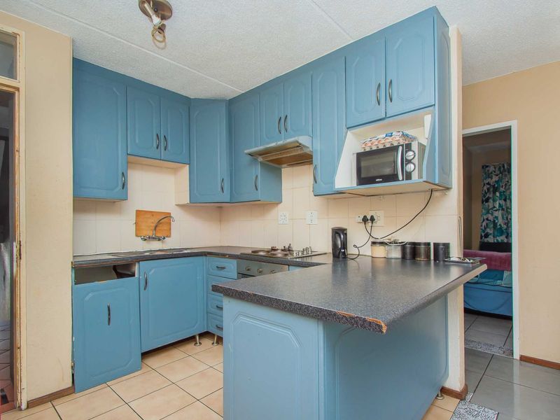 A dated kitchen featuring blue cabinetry, laminate countertops, and a built-in hob, offering potential for a modern renovation.