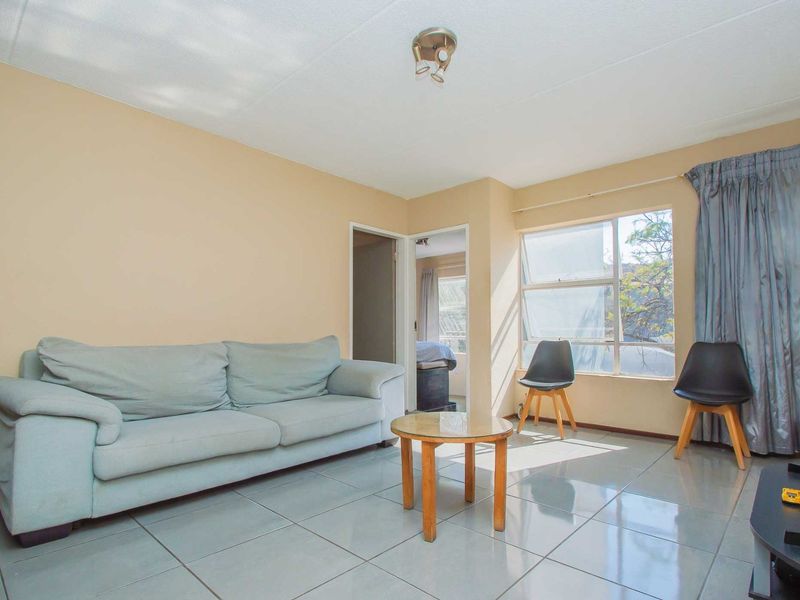 A living room featuring tiled flooring, neutral wall paint, and a large window allowing natural light into the space.