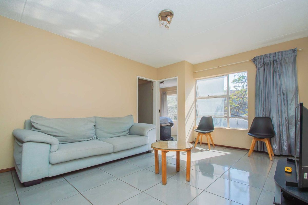 A living room featuring tiled flooring, neutral wall paint, and a large window allowing natural light into the space.