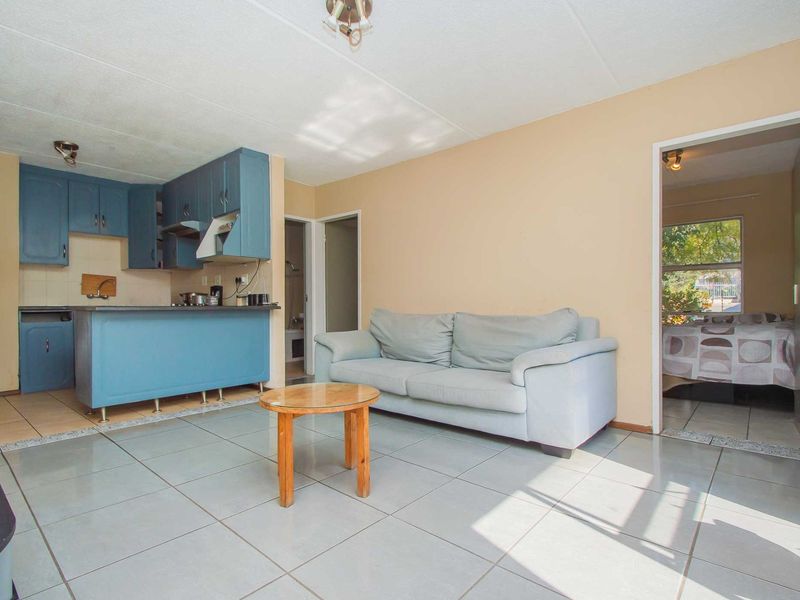 Open-plan living area featuring tiled flooring and a compact kitchen with blue cabinetry, providing a functional layout with direct access to the bedroom.