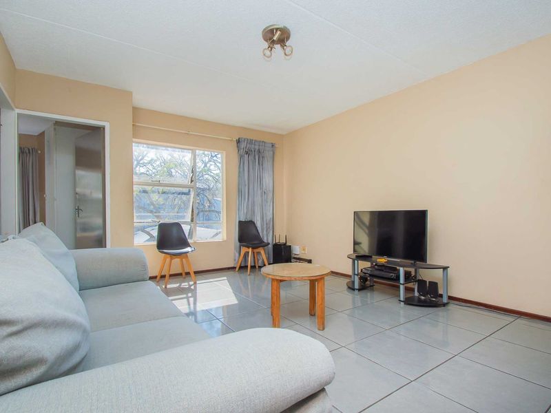 A functional living room featuring neutral wall tones, tiled flooring, and a large window allowing for natural light.