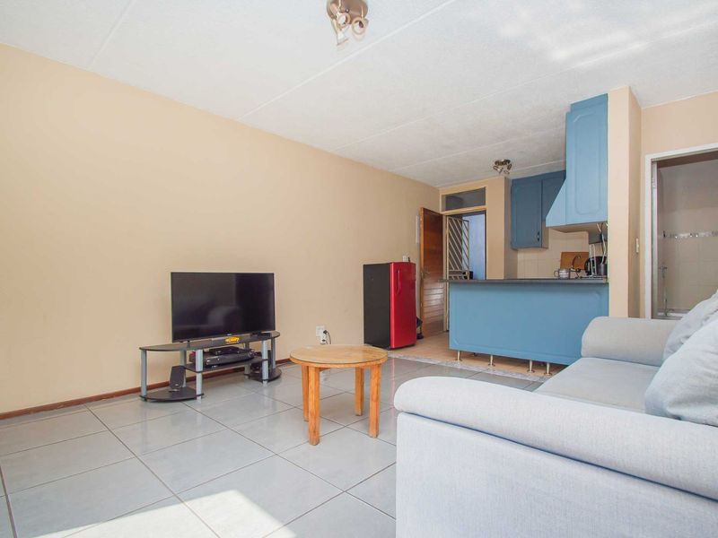 Open-plan living area featuring tiled flooring and a compact kitchen with blue cabinetry and an integrated extractor fan.