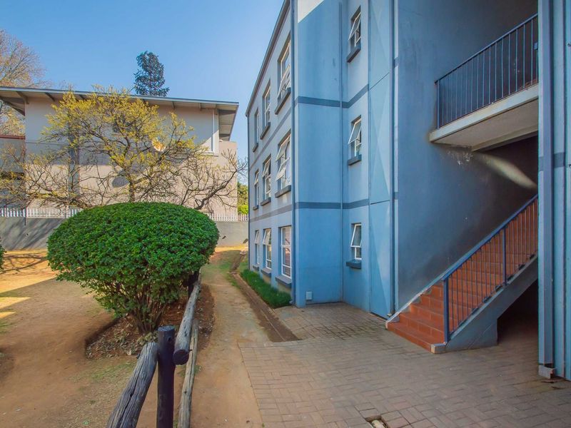 Rear view of the apartment building featuring an external staircase, paved walkway, and landscaped garden area.