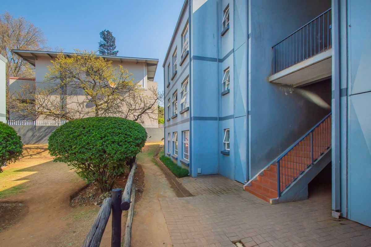 Rear view of the apartment building featuring an external staircase, paved walkway, and landscaped garden area.