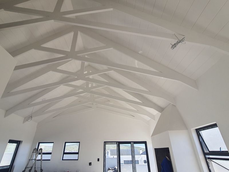 Spacious living area featuring a high vaulted ceiling with exposed white timber trusses, modern aluminium windows, and large sliding doors leading outdoors.