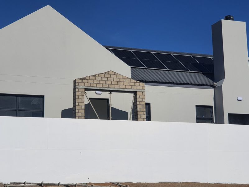 Rear view of a modern house featuring a metal roof, installed solar panels, a prominent chimney, and a clean white boundary wall.