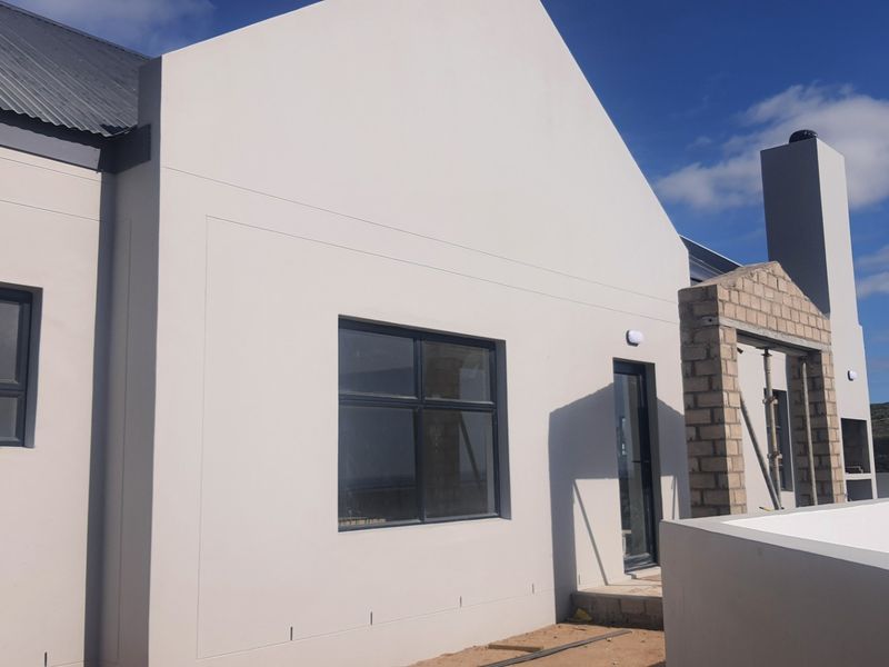 Rear elevation of a modern home featuring a gabled roof, aluminium windows, and an unfinished outdoor fireplace structure.