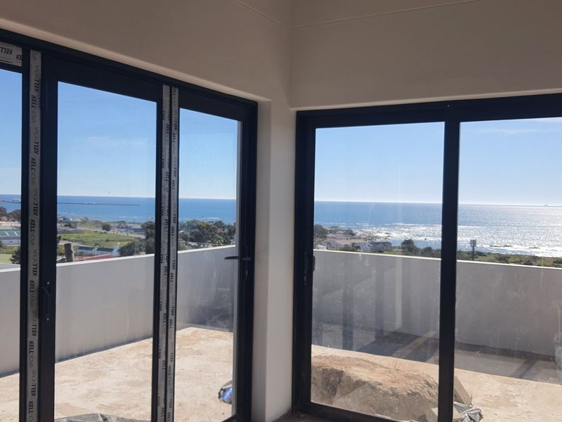 An empty living area featuring large black aluminium sliding doors that open onto a balcony with expansive ocean views.