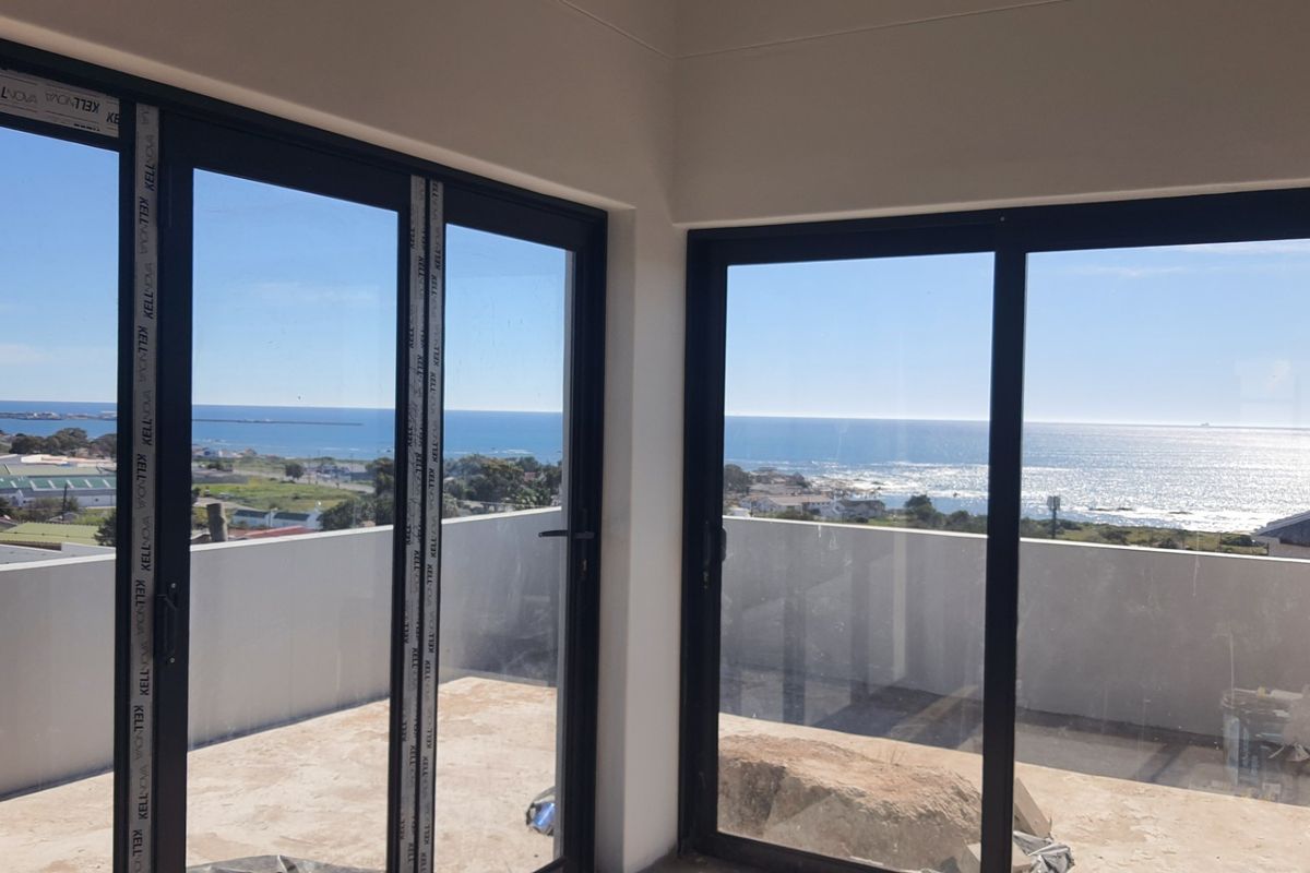 An empty living area featuring large black aluminium sliding doors that open onto a balcony with expansive ocean views.