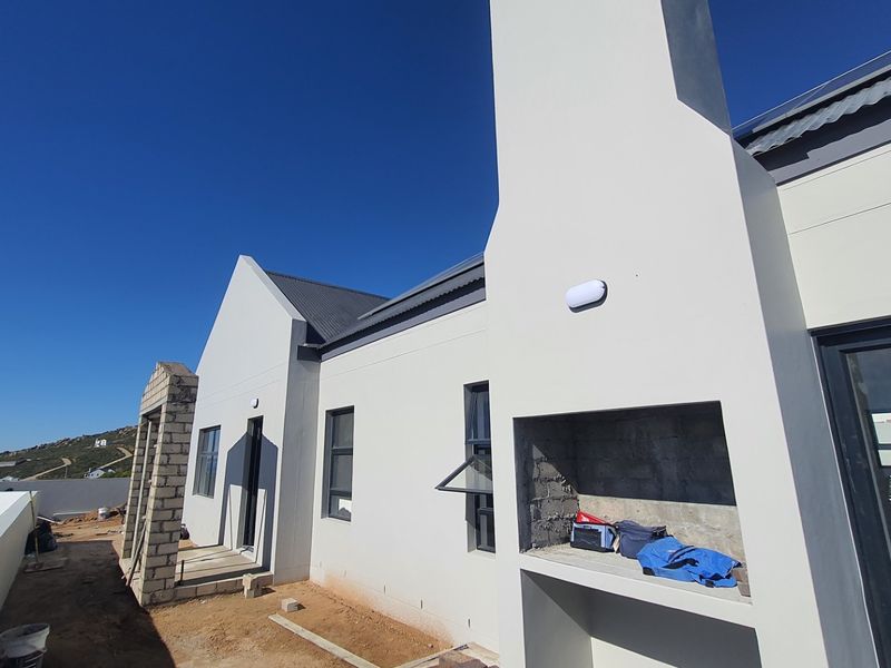 Rear exterior view of a modern house featuring a built-in braai, metal roofing, and aluminium window frames, currently in the final stages of construction.