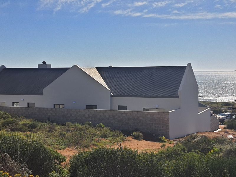 Rear view of a modern coastal home featuring a corrugated metal roof and a masonry boundary wall overlooking the ocean.